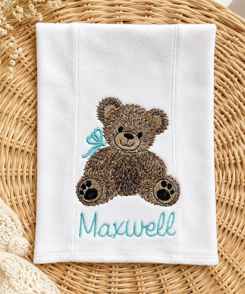 White burp cloth with embroidered teddy bear and the name Maxwell in blue