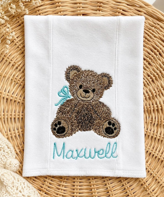 White burp cloth with embroidered teddy bear and the name Maxwell in blue