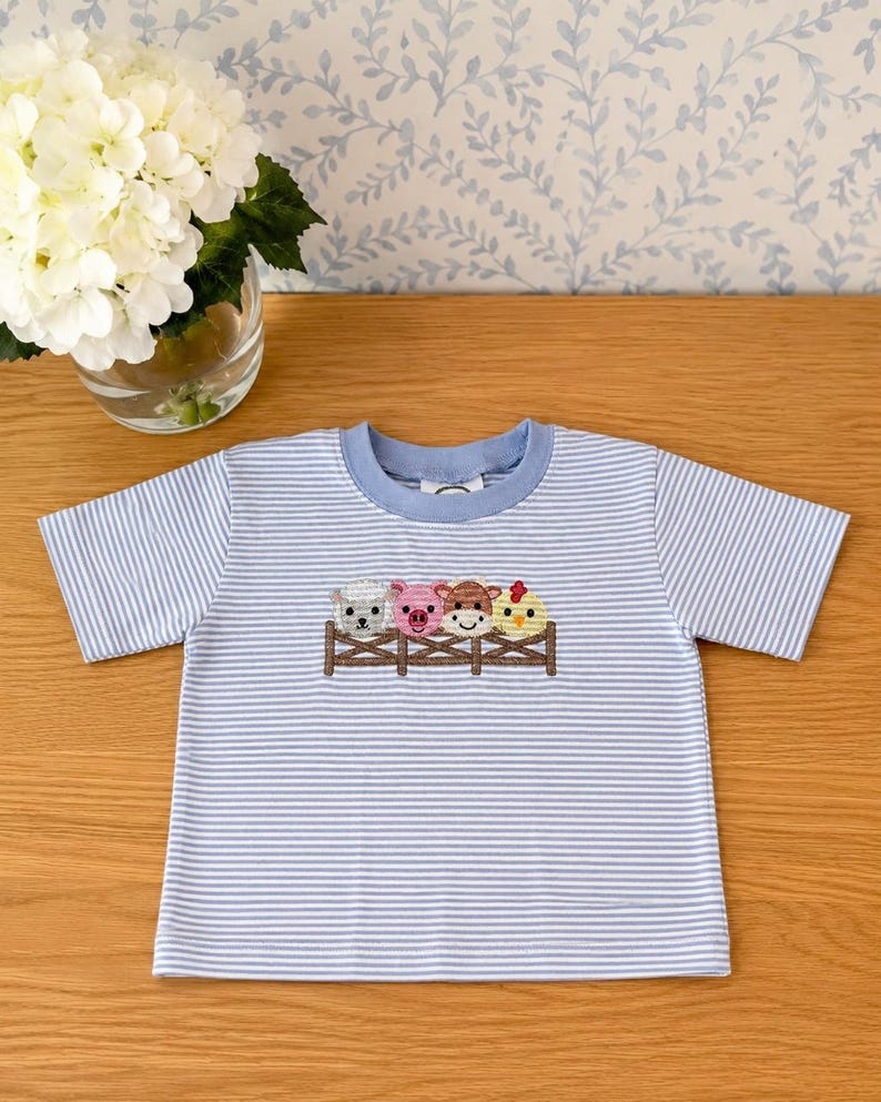 Striped toddler shirt embroidered with farm animals at a fence