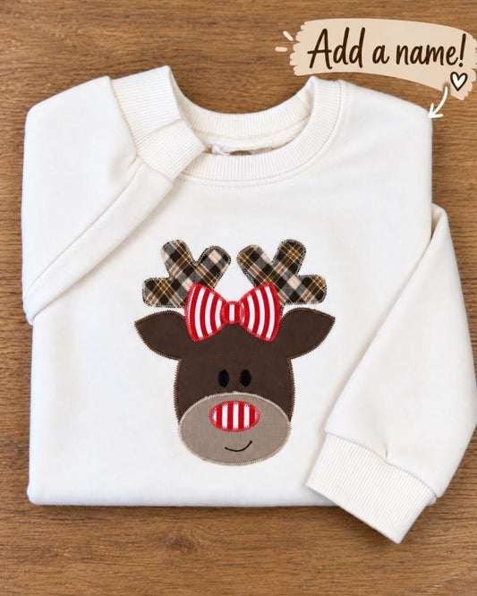 Toddler crewneck with a handmade plaid reindeer appliqué wearing a striped bow